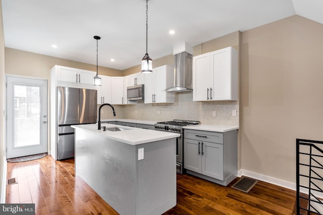 kitchen with appliances with stainless steel finishes, dark hardwood / wood-style floors, sink, a center island with sink, and wall chimney range hood