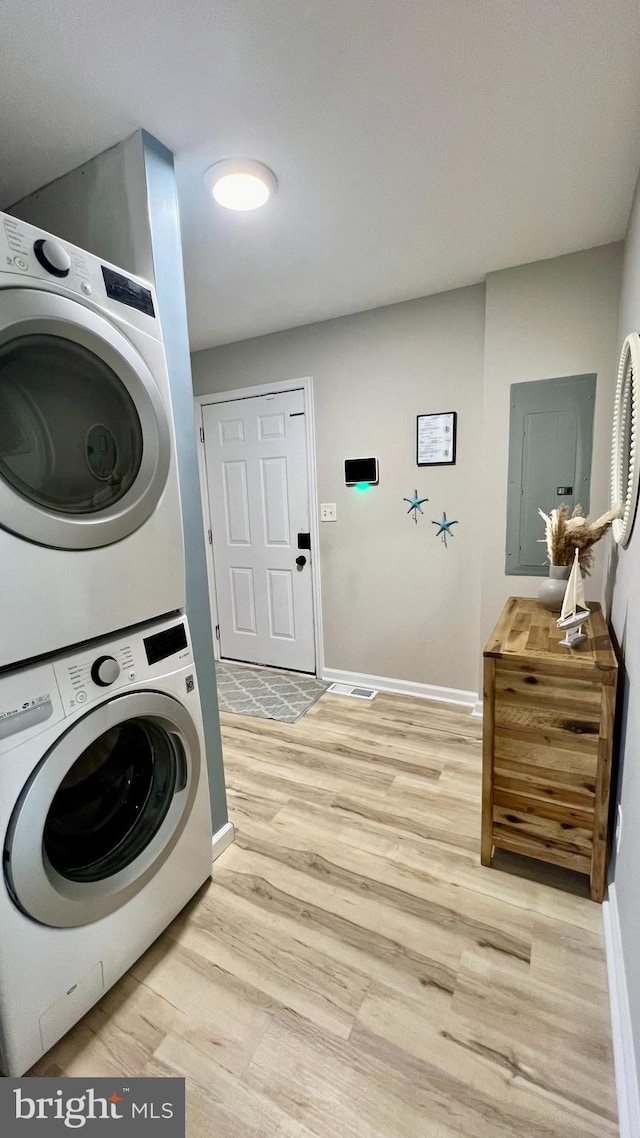 washroom featuring electric panel, stacked washer and clothes dryer, and light hardwood / wood-style floors