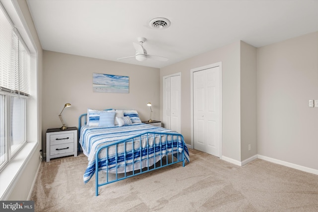 carpeted bedroom featuring a ceiling fan, baseboards, visible vents, and two closets