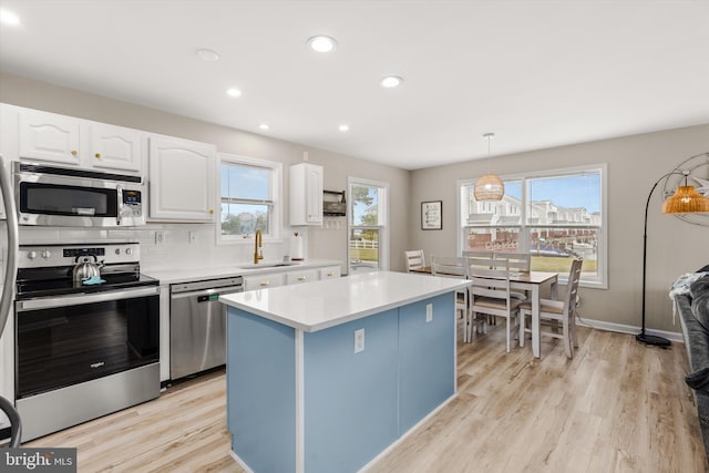 kitchen with hanging light fixtures, appliances with stainless steel finishes, white cabinets, and light hardwood / wood-style floors