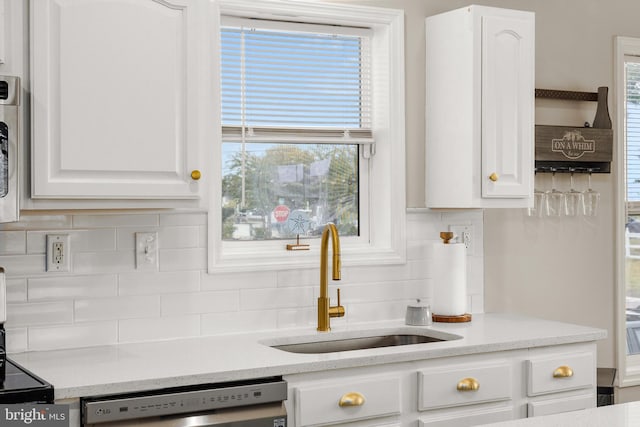 kitchen featuring white cabinetry, dishwasher, sink, light stone countertops, and decorative backsplash