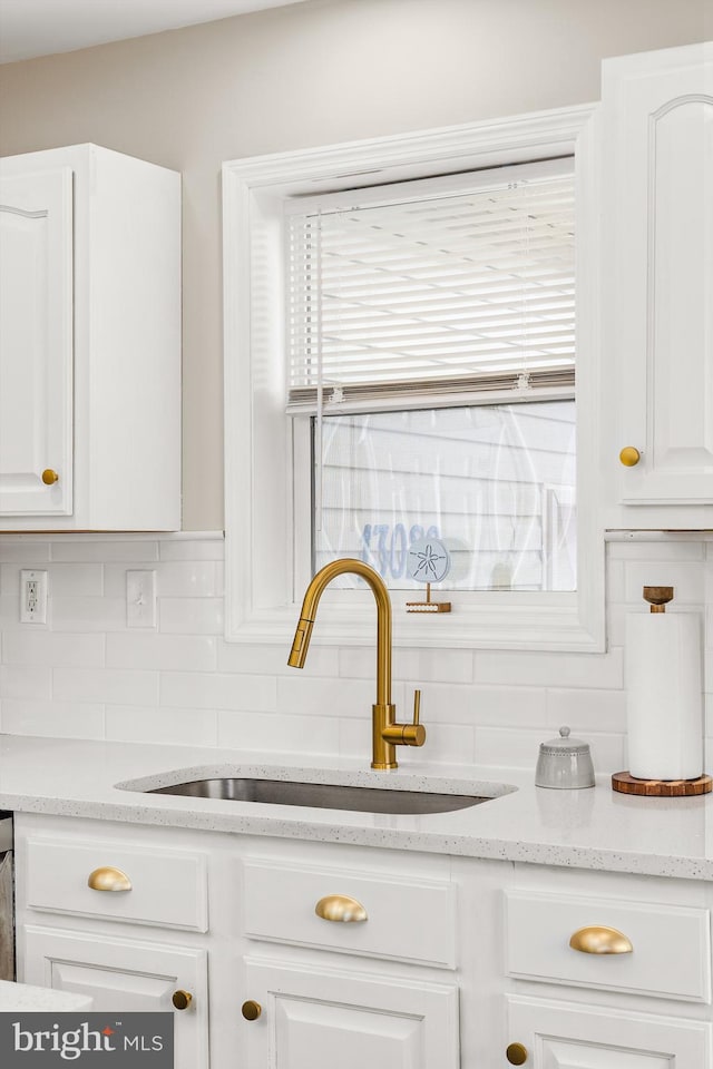 kitchen with light stone counters, white cabinetry, backsplash, and sink