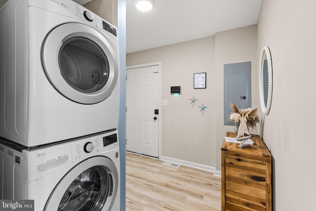 clothes washing area with visible vents, light wood-type flooring, stacked washer and dryer, electric panel, and baseboards