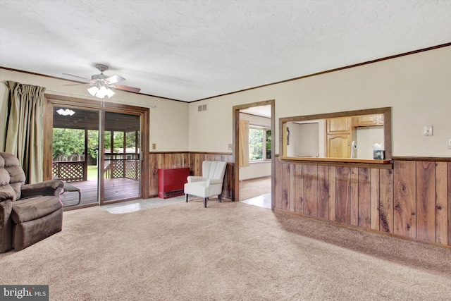 carpeted living room with a textured ceiling, wooden walls, ceiling fan, and a wealth of natural light