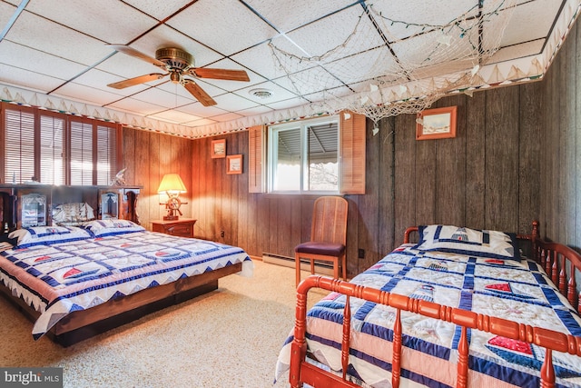 carpeted bedroom featuring ceiling fan, wooden walls, a paneled ceiling, and a baseboard radiator