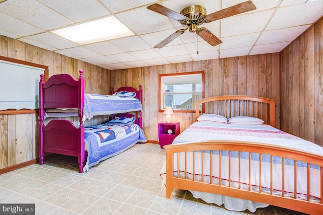 bedroom with ceiling fan, a drop ceiling, tile patterned floors, and wood walls