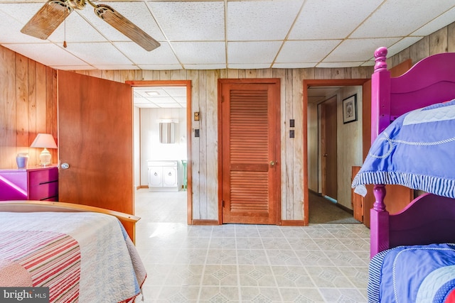 bedroom with a closet, wooden walls, a ceiling fan, and a drop ceiling