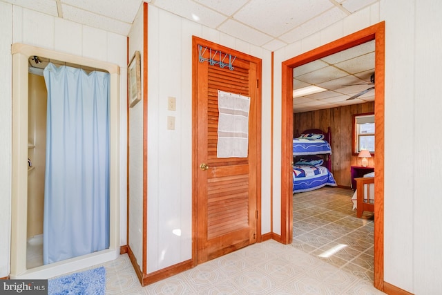 hall with tile patterned flooring, wood walls, and a paneled ceiling