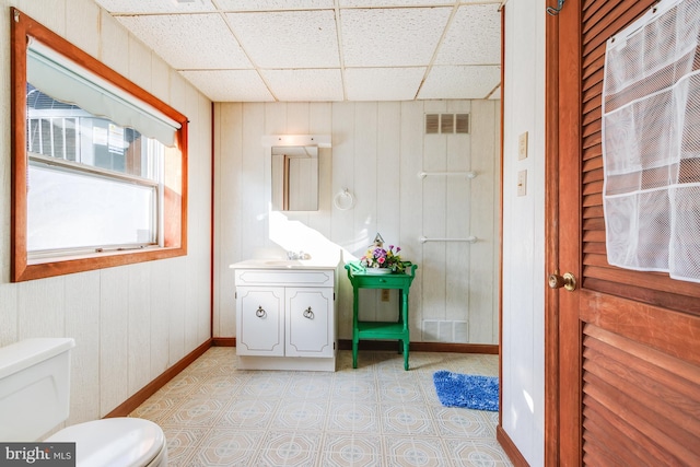 half bathroom featuring a drop ceiling, toilet, vanity, visible vents, and baseboards