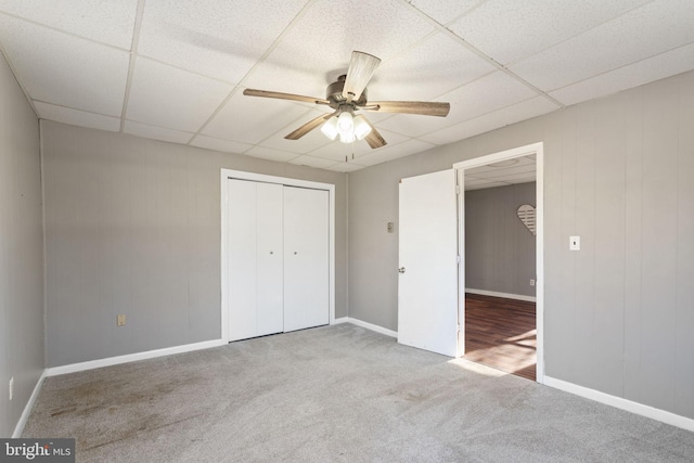 unfurnished bedroom with a drop ceiling, a closet, carpet floors, baseboards, and ceiling fan