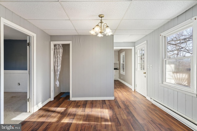 interior space featuring wood finished floors, baseboards, a drop ceiling, a baseboard heating unit, and a notable chandelier