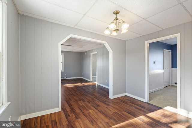 spare room with arched walkways, a notable chandelier, a paneled ceiling, and wood finished floors