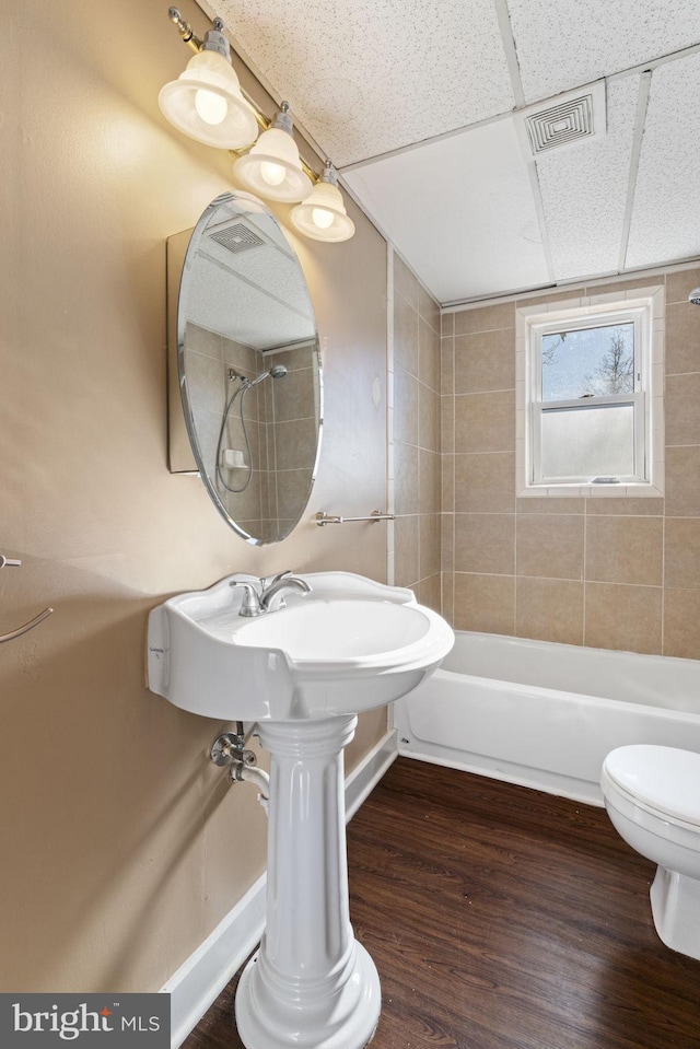 full bath featuring wood finished floors, visible vents, tub / shower combination, a drop ceiling, and toilet