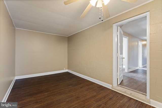 spare room with a ceiling fan, baseboards, dark wood-type flooring, and concrete block wall