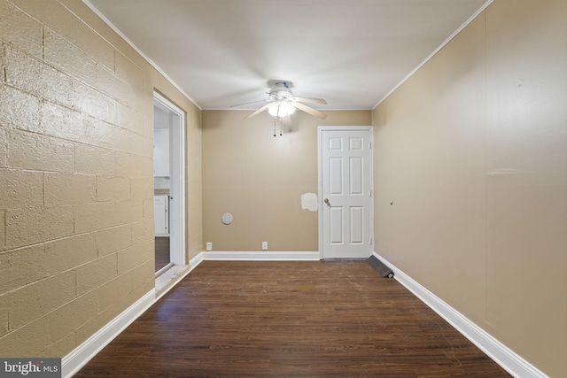 empty room with concrete block wall, a ceiling fan, baseboards, dark wood-style flooring, and crown molding