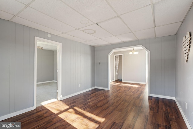 spare room featuring wood finished floors, baseboards, arched walkways, a drop ceiling, and a notable chandelier