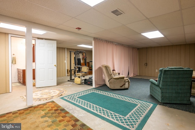 finished basement featuring a drop ceiling, visible vents, and wooden walls