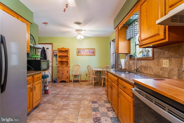 kitchen featuring tasteful backsplash, visible vents, freestanding refrigerator, under cabinet range hood, and a sink