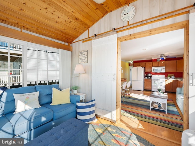 living room featuring light wood-type flooring, wooden walls, ceiling fan, vaulted ceiling, and a barn door