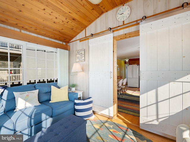 living room with wooden walls, wood ceiling, lofted ceiling, a barn door, and light wood-type flooring