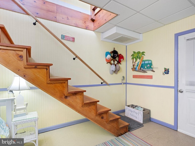 stairs with a drop ceiling, wooden walls, and a skylight