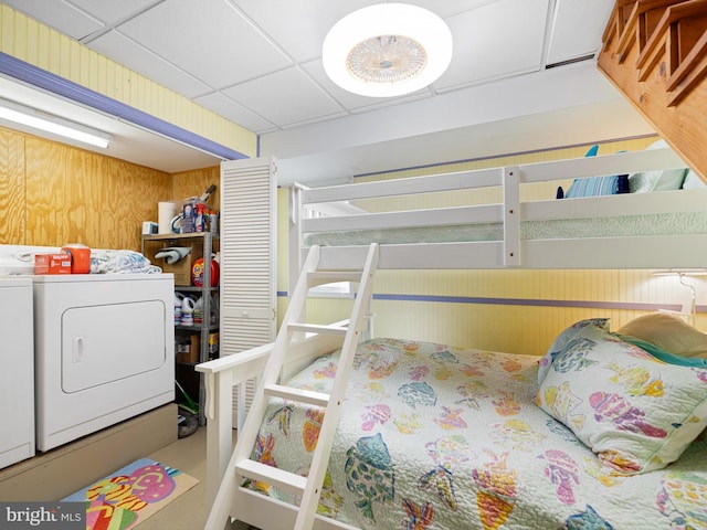 bedroom featuring wood walls, a drop ceiling, and washer and clothes dryer