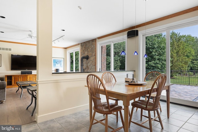 dining room with rail lighting, ceiling fan, crown molding, light hardwood / wood-style flooring, and a wood stove