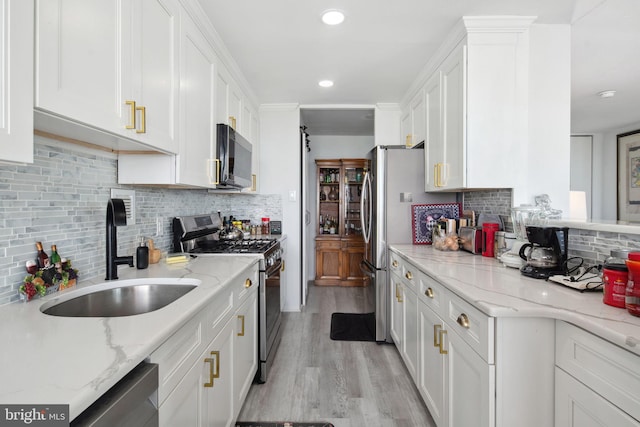 kitchen featuring white cabinets, appliances with stainless steel finishes, light stone counters, and sink