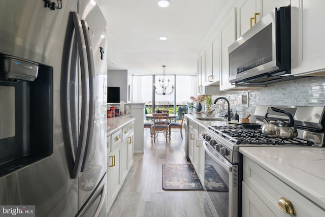 kitchen with light wood-type flooring, a notable chandelier, white cabinetry, stainless steel appliances, and sink