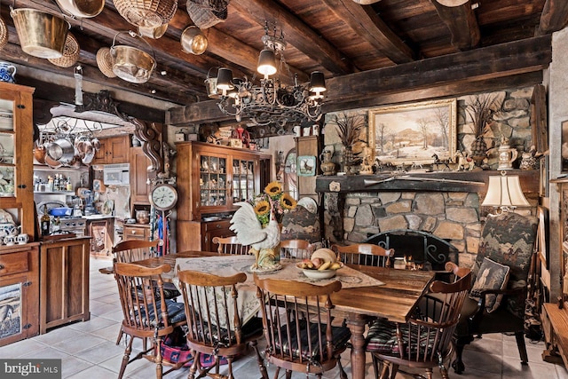 tiled dining area featuring beamed ceiling, a stone fireplace, wood ceiling, and an inviting chandelier