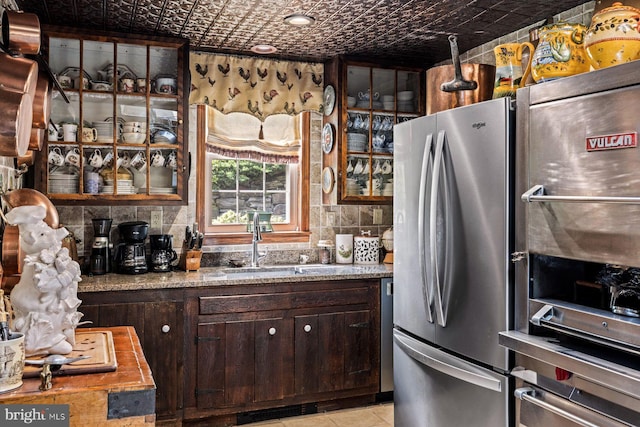 kitchen featuring backsplash, dark brown cabinetry, sink, light tile patterned floors, and stainless steel fridge