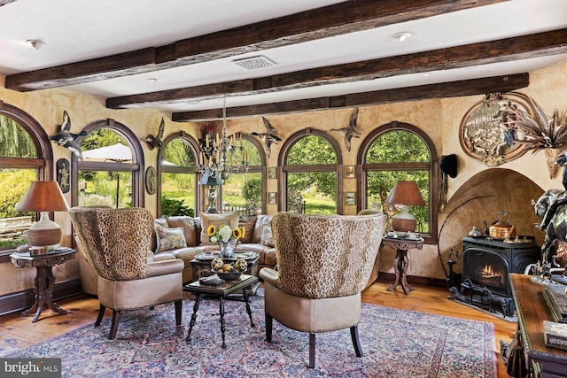 living room featuring light hardwood / wood-style floors, an inviting chandelier, beamed ceiling, and a wood stove