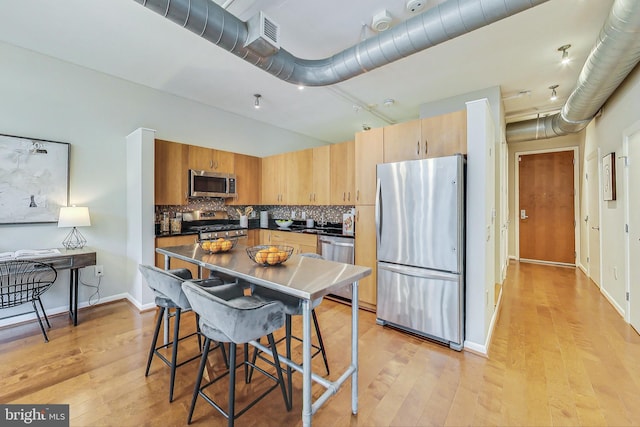 kitchen with light hardwood / wood-style flooring, backsplash, and appliances with stainless steel finishes