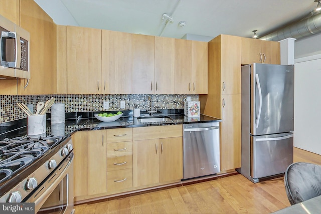 kitchen with dark stone countertops, light brown cabinetry, decorative backsplash, appliances with stainless steel finishes, and light hardwood / wood-style floors