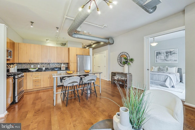 kitchen with backsplash, stainless steel appliances, a center island, light brown cabinets, and light hardwood / wood-style floors