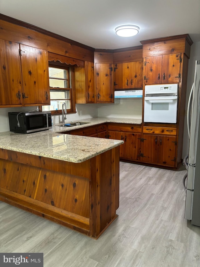 kitchen with kitchen peninsula, fridge, light hardwood / wood-style floors, and oven