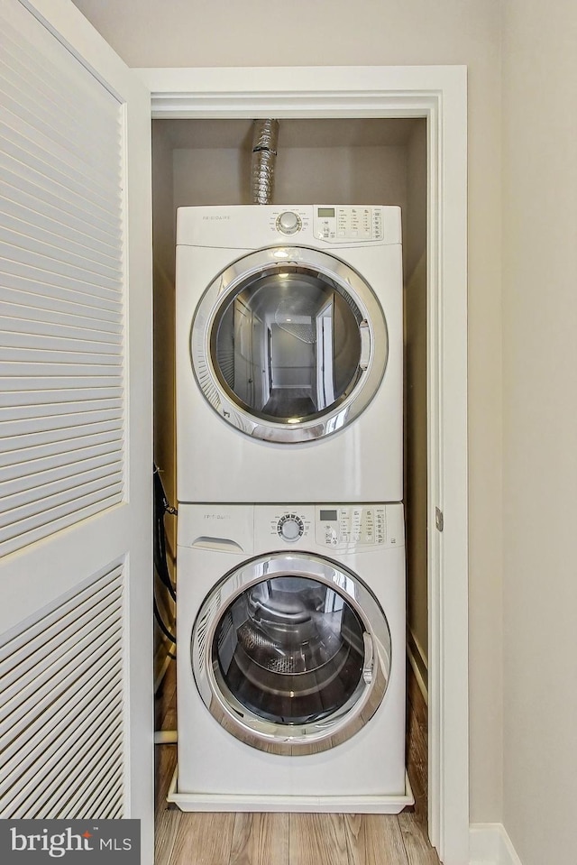 laundry room with stacked washer and clothes dryer and light hardwood / wood-style floors