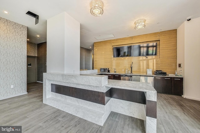 kitchen with dark brown cabinetry, appliances with stainless steel finishes, light hardwood / wood-style flooring, and kitchen peninsula