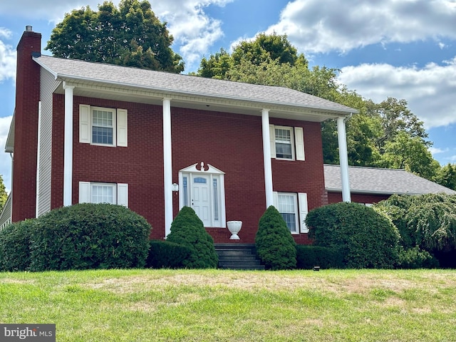 view of front facade featuring brick siding, roof with shingles, a chimney, and a front yard