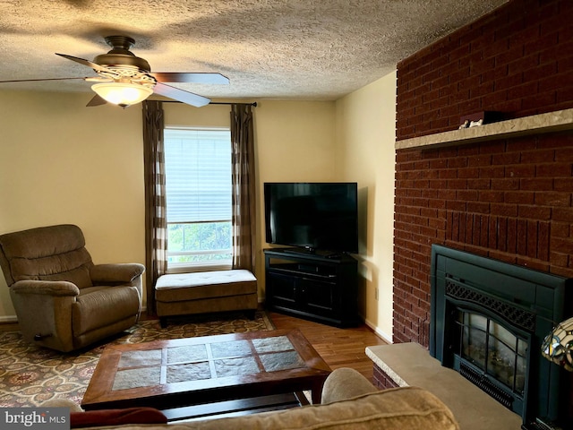 living room featuring ceiling fan, wood-type flooring, a textured ceiling, and a fireplace