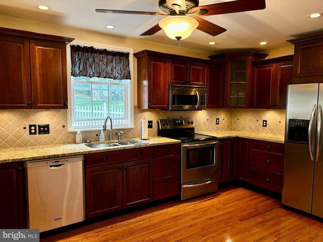 kitchen featuring stainless steel appliances, light hardwood / wood-style flooring, tasteful backsplash, sink, and ceiling fan