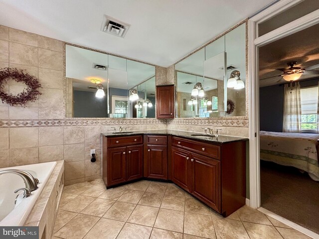 bathroom featuring tile walls, vanity, tiled tub, ceiling fan, and tile patterned flooring