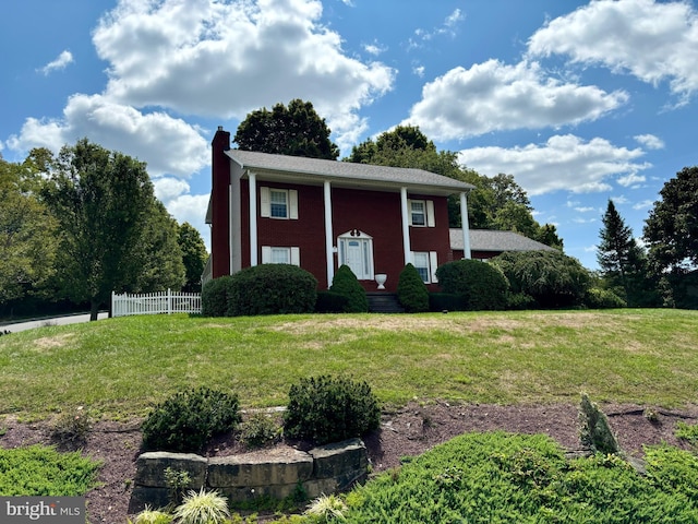 neoclassical / greek revival house with a chimney, fence, and a front yard