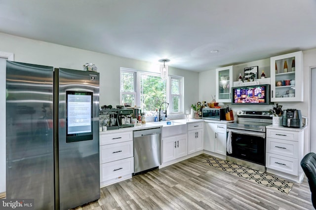 kitchen with appliances with stainless steel finishes, light hardwood / wood-style floors, sink, white cabinets, and hanging light fixtures