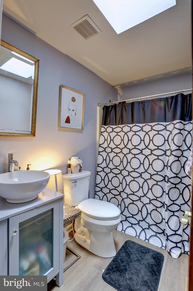 bathroom with hardwood / wood-style flooring, a skylight, vanity, curtained shower, and toilet