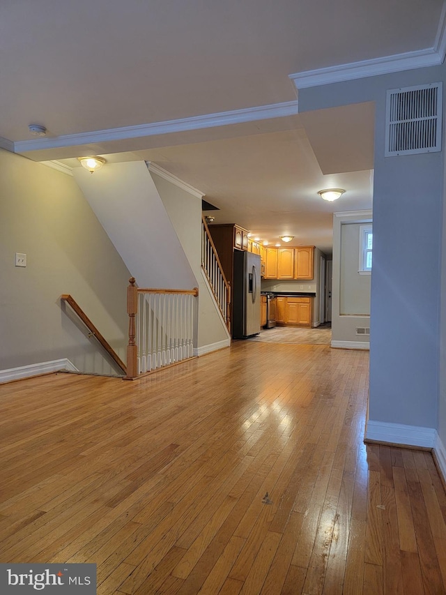 unfurnished living room featuring crown molding, visible vents, light wood-style flooring, baseboards, and stairs