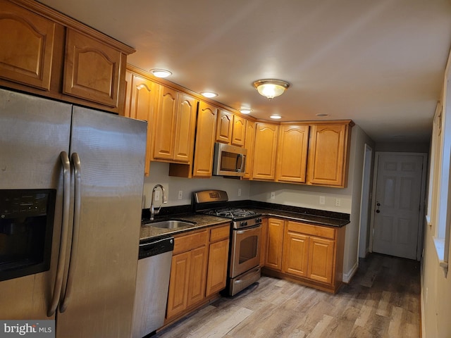 kitchen with stainless steel appliances, light wood-type flooring, brown cabinetry, and a sink