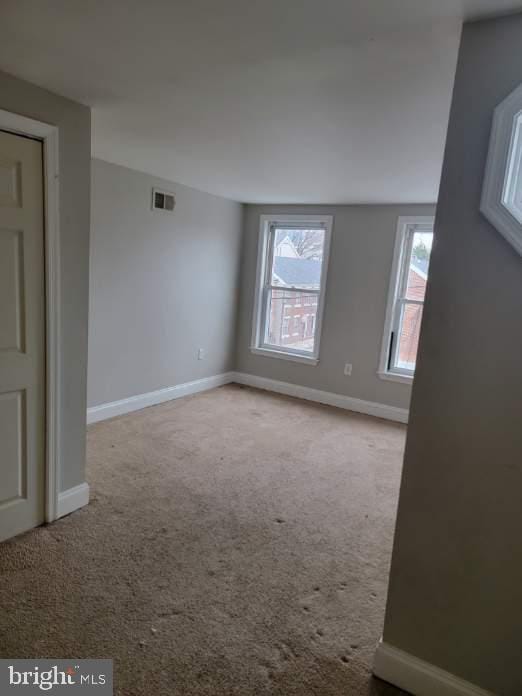 empty room featuring light carpet, visible vents, and baseboards