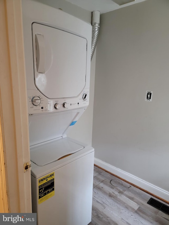 washroom featuring stacked washer and clothes dryer, light wood finished floors, visible vents, laundry area, and baseboards