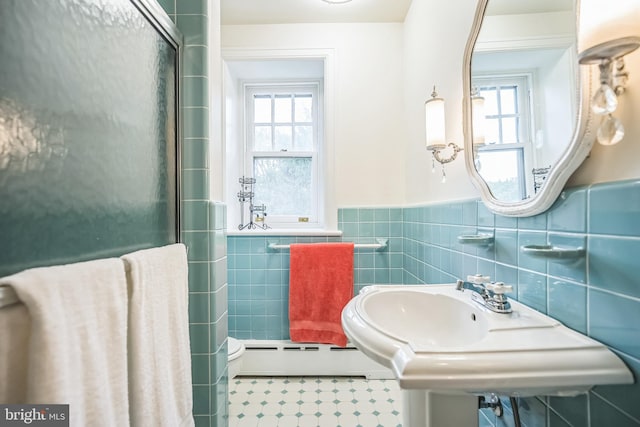 bathroom featuring a baseboard heating unit, plenty of natural light, walk in shower, and sink